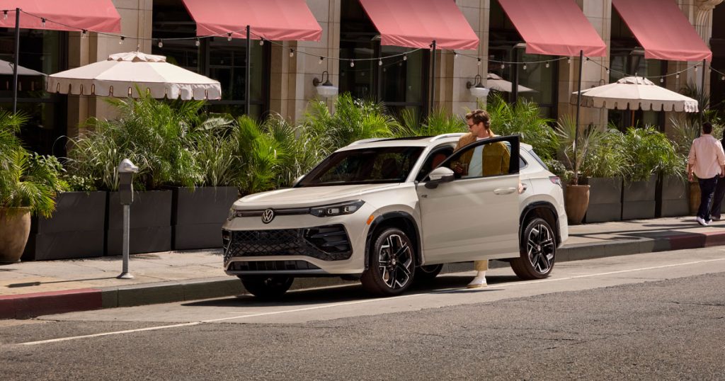 A man enters the new 2025 VW Tiguan SUV as it sits parked outside of a restaurant.